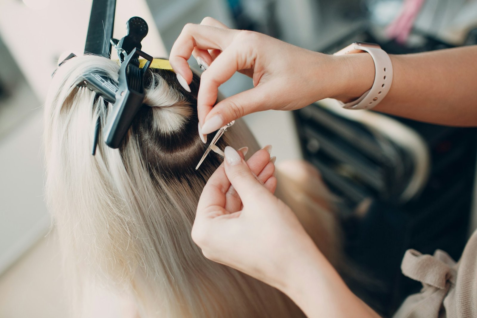 Hairdresser female making hair extensions to young woman with blonde hair in beauty salon.